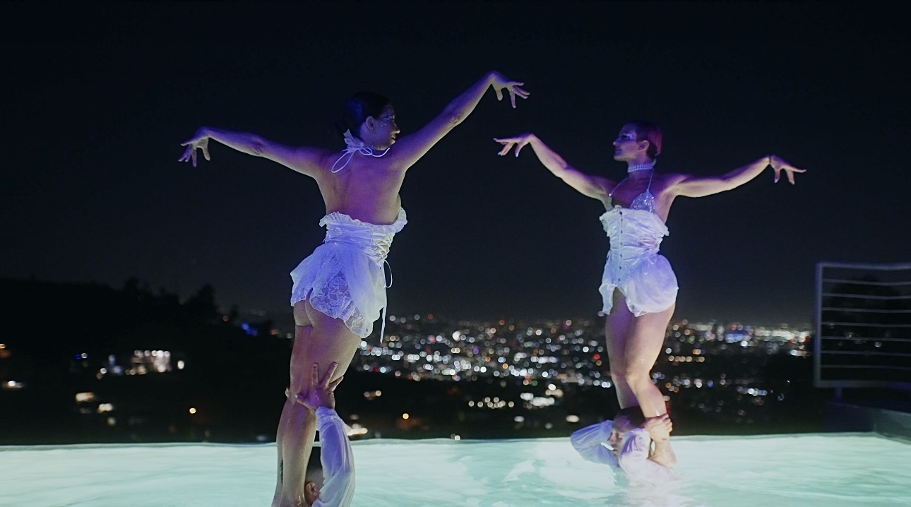 Two dancers performing in a swimming pool at night above the Los Angeles lights